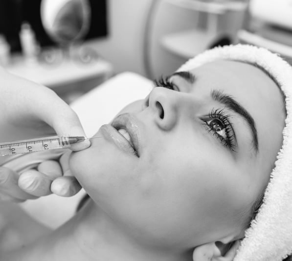 The doctor cosmetologist makes the Rejuvenating facial injections procedure for tightening and smoothing wrinkles on the face skin of a beautiful, young woman in a beauty salon. The hands of cosmetologist are close-ups that inject hyaluronic acid into the lips of the woman.